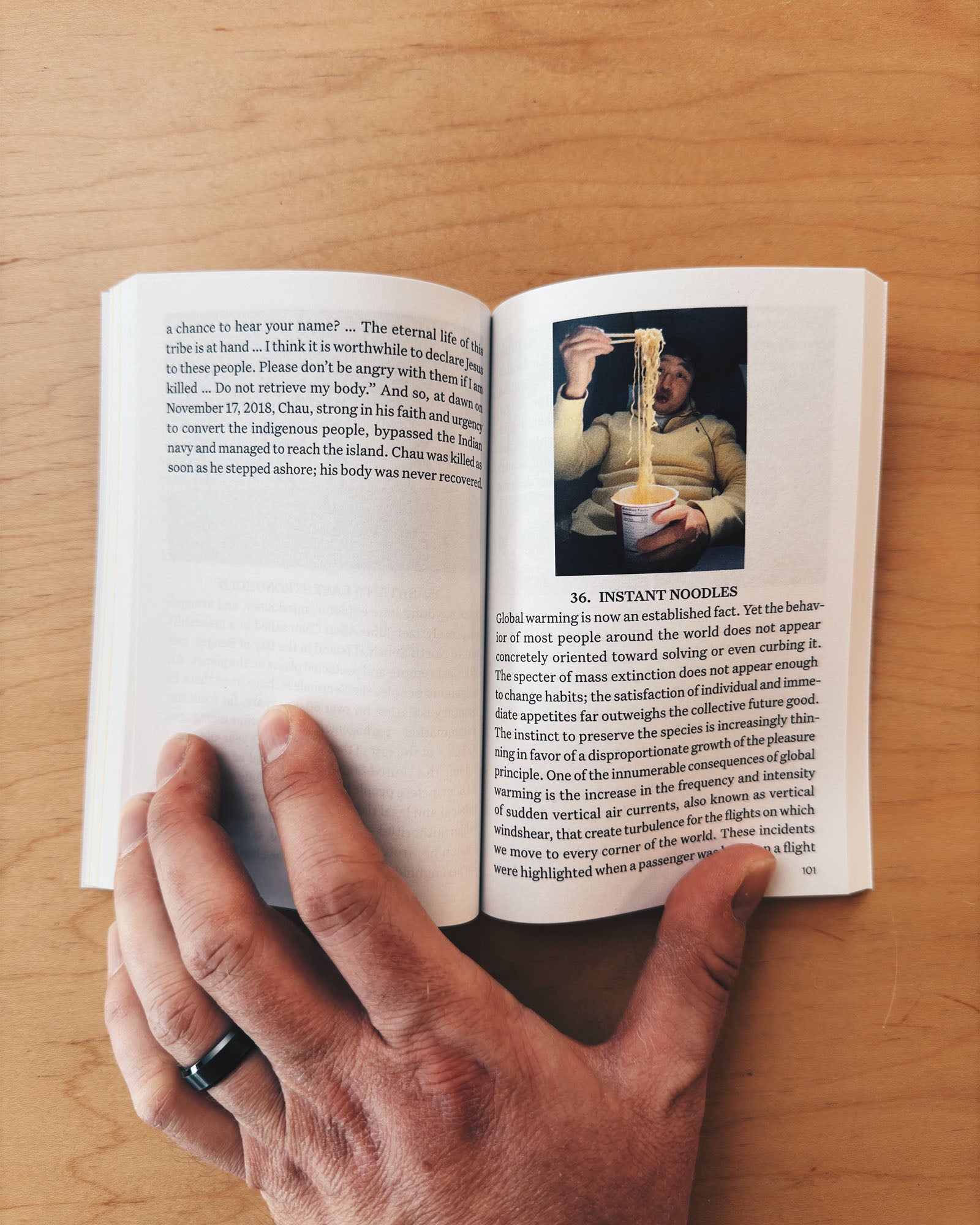 Hand holding an open book with a page showing a picture of a person eating instant noodles.