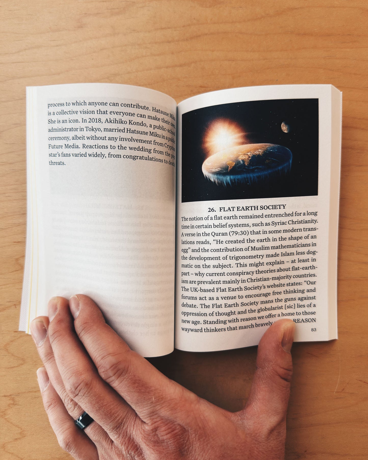 Open book on a wooden surface with a hand holding it, displaying an image of a flat Earth.