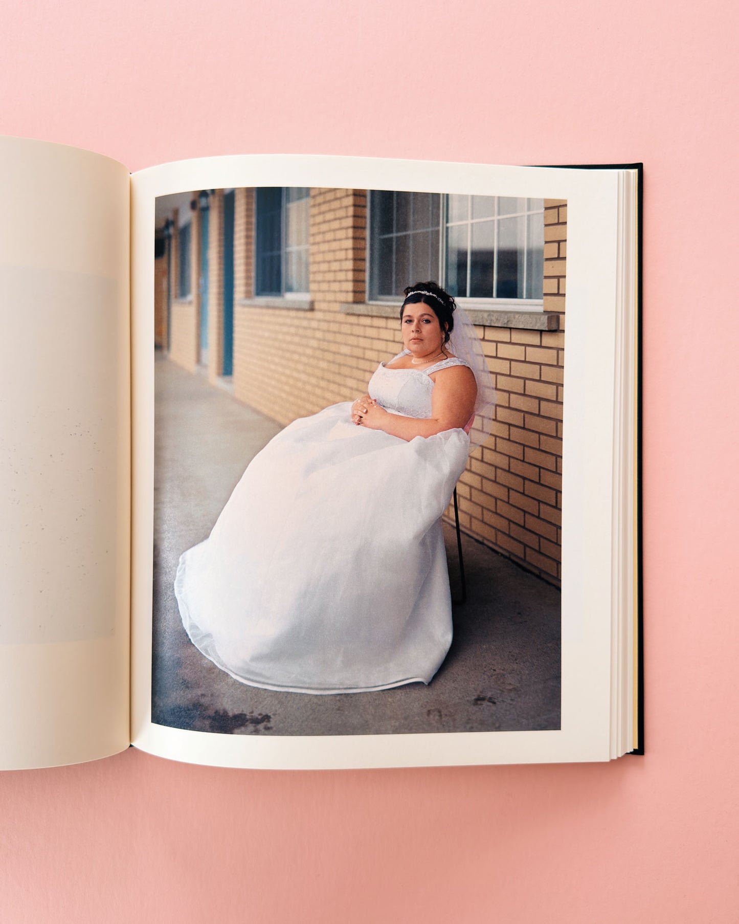 Open photo album showing a bride in a white gown against a brick wall. Classic photo book Niagara by Alec Soth. Made with large format film photography.