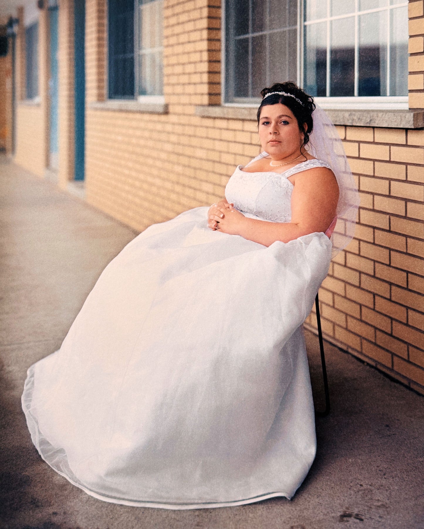 Person in a white wedding dress sitting on a chair against a brick wall.