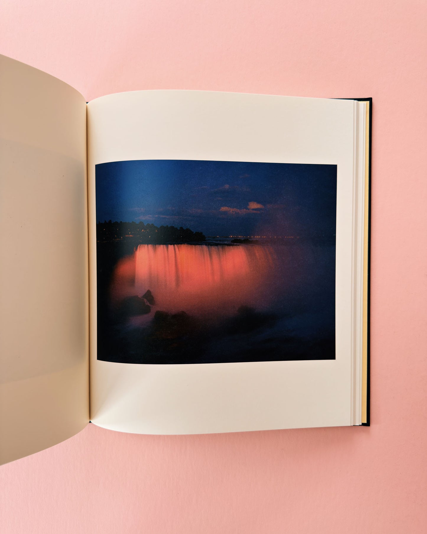 Open book displaying a photograph of a sunset over water on a pink background